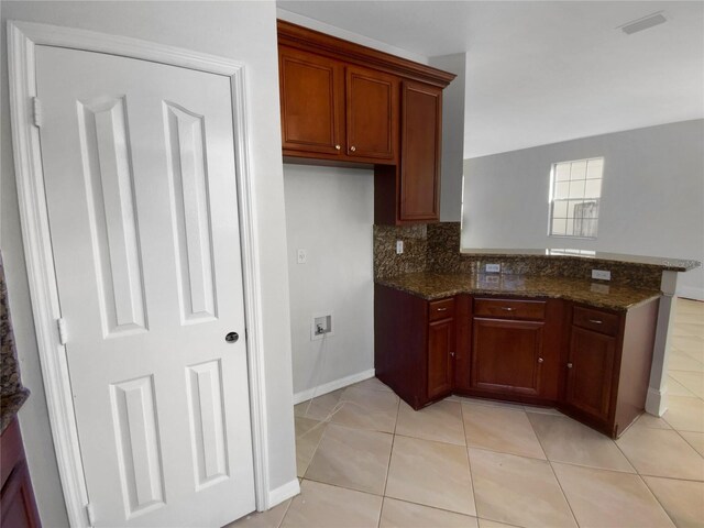 kitchen featuring light tile patterned floors, backsplash, and dark stone counters