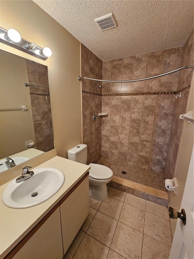 bathroom with vanity, tiled shower, toilet, tile patterned floors, and a textured ceiling