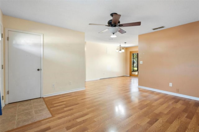 spare room featuring ceiling fan with notable chandelier and light hardwood / wood-style flooring