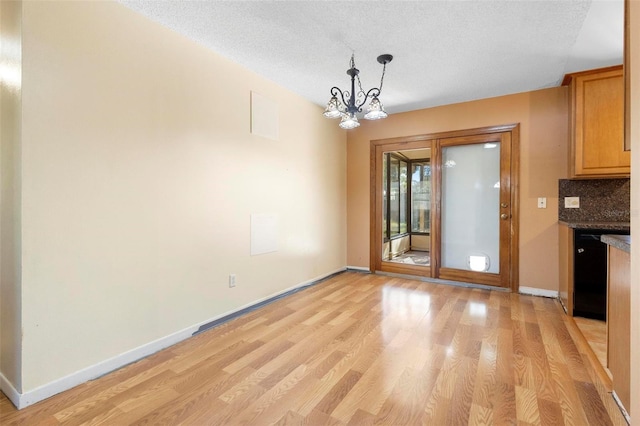 unfurnished dining area featuring a textured ceiling, light hardwood / wood-style floors, and a notable chandelier