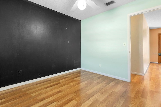 unfurnished room with a textured ceiling, light wood-type flooring, and ceiling fan