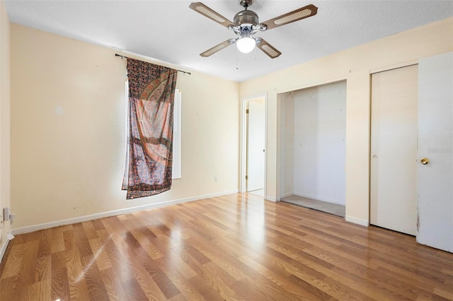 unfurnished bedroom featuring multiple closets, ceiling fan, a textured ceiling, and light wood-type flooring