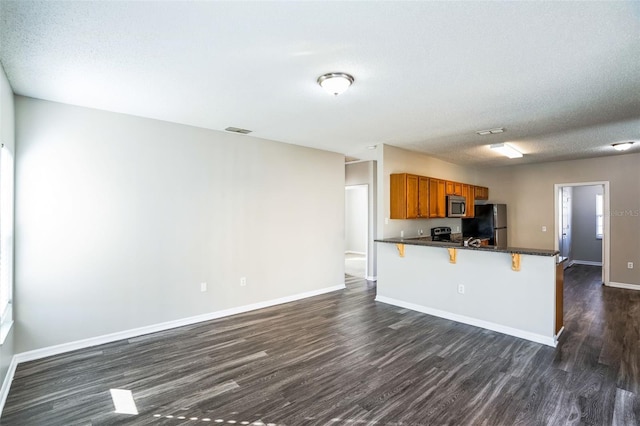 kitchen with kitchen peninsula, appliances with stainless steel finishes, a breakfast bar, a textured ceiling, and dark wood-type flooring