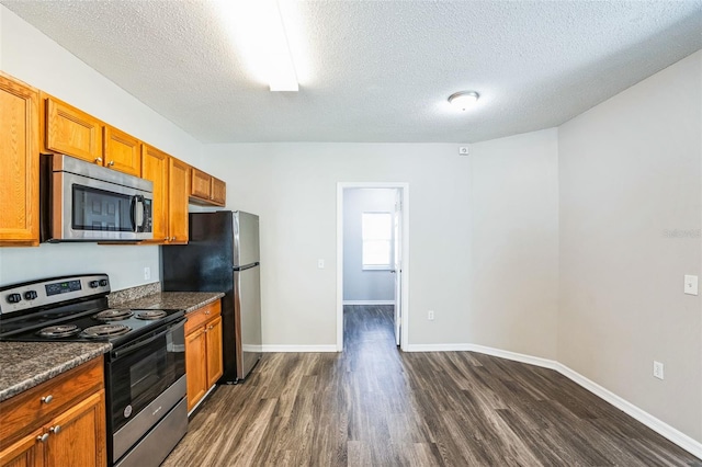 kitchen with dark hardwood / wood-style flooring, a textured ceiling, appliances with stainless steel finishes, and dark stone counters