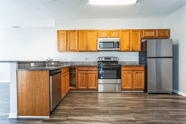 kitchen featuring sink, dark hardwood / wood-style floors, dark stone countertops, a textured ceiling, and appliances with stainless steel finishes