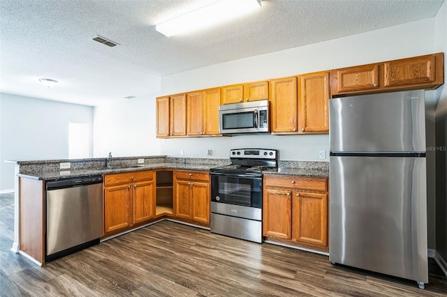 kitchen featuring dark wood-type flooring, sink, a textured ceiling, kitchen peninsula, and stainless steel appliances