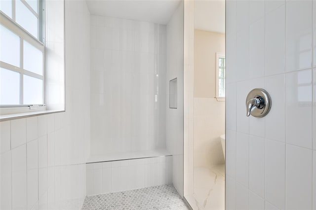 bathroom featuring a tile shower, a wealth of natural light, and tile walls