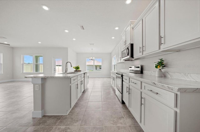 kitchen featuring light tile patterned flooring, sink, white cabinets, stainless steel appliances, and a center island with sink