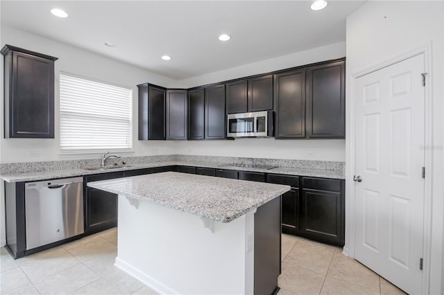 kitchen with sink, appliances with stainless steel finishes, a kitchen island, light stone counters, and dark brown cabinetry