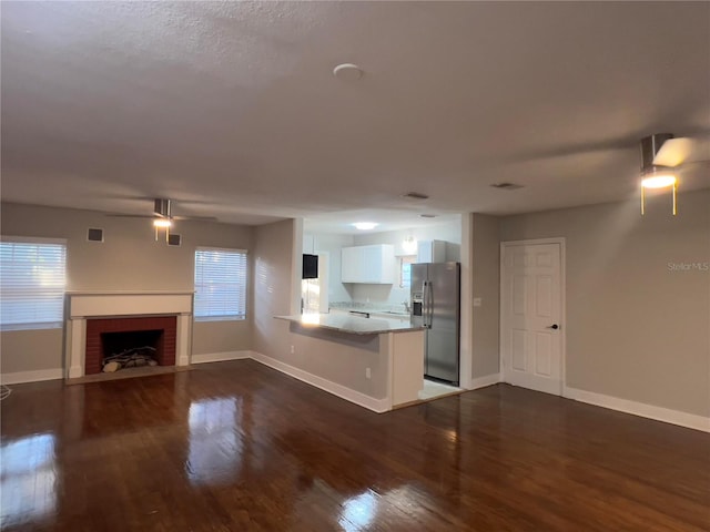 kitchen with a wealth of natural light, dark wood-type flooring, stainless steel refrigerator with ice dispenser, kitchen peninsula, and white cabinets