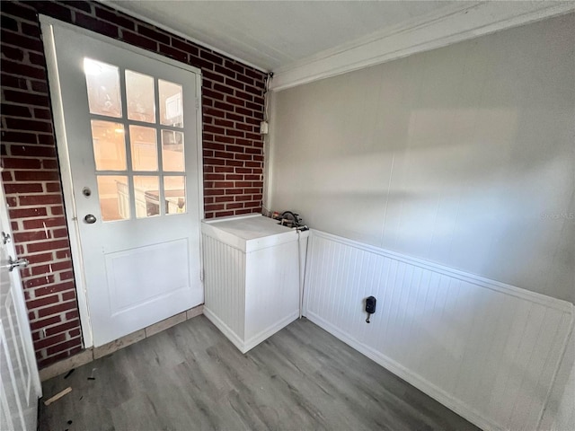 entryway featuring light wood-type flooring, crown molding, and brick wall