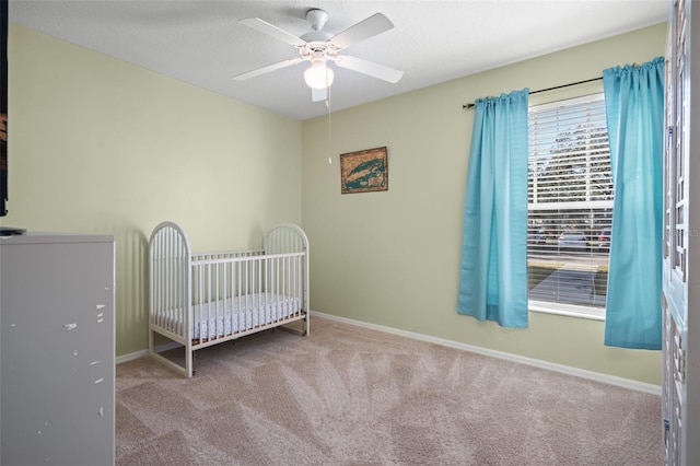 unfurnished bedroom with light carpet, a nursery area, and ceiling fan