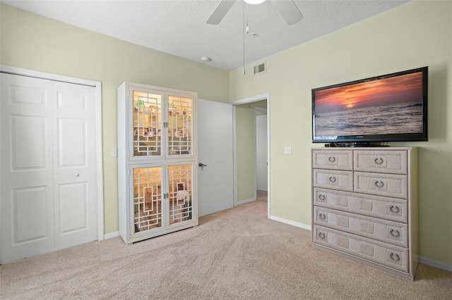 unfurnished bedroom featuring ceiling fan, a closet, light carpet, and a textured ceiling