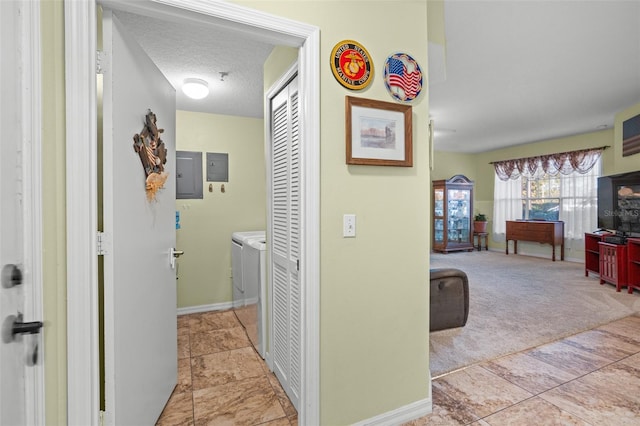 hallway with light carpet, a textured ceiling, electric panel, and washer and clothes dryer