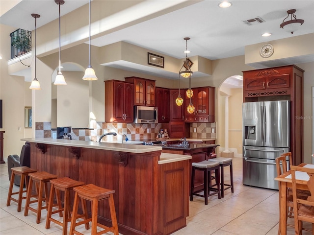 kitchen featuring stainless steel appliances, kitchen peninsula, pendant lighting, a kitchen bar, and decorative backsplash