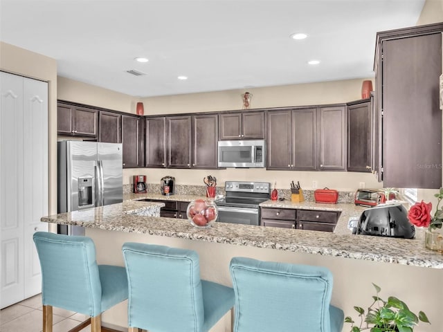 kitchen featuring light tile patterned floors, light stone counters, dark brown cabinetry, and appliances with stainless steel finishes