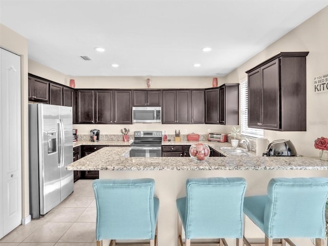 kitchen featuring sink, kitchen peninsula, a kitchen bar, light tile patterned floors, and appliances with stainless steel finishes