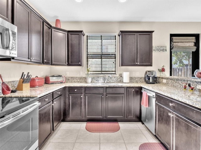 kitchen featuring light stone countertops, dark brown cabinets, stainless steel appliances, sink, and light tile patterned floors