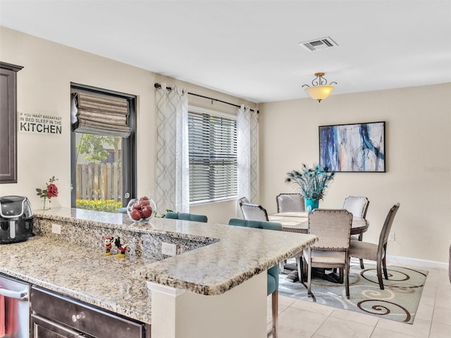 kitchen featuring dark brown cabinets, a kitchen bar, light tile patterned floors, and light stone counters