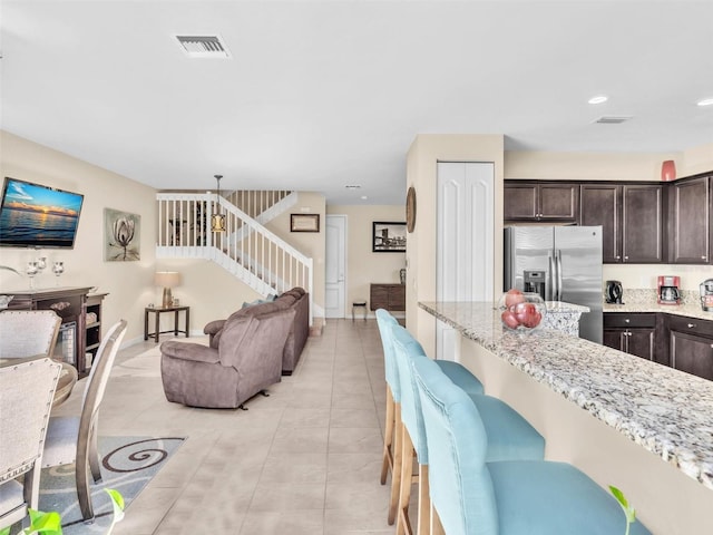 kitchen with light stone countertops, stainless steel fridge, dark brown cabinetry, and pendant lighting