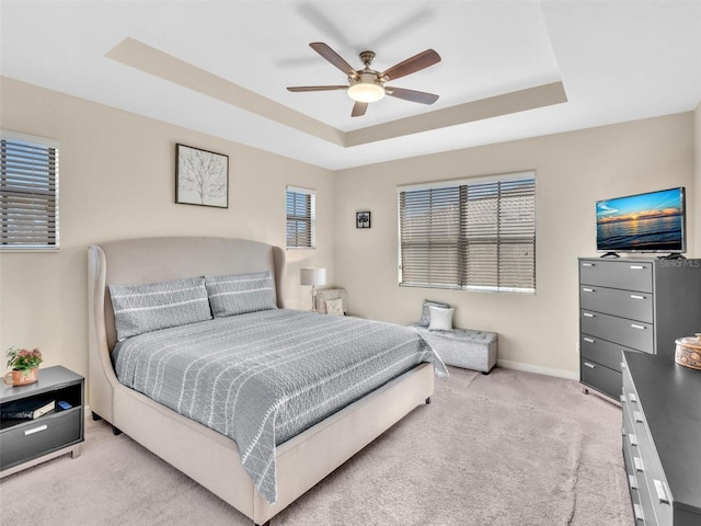 bedroom with ceiling fan, a raised ceiling, light colored carpet, and multiple windows