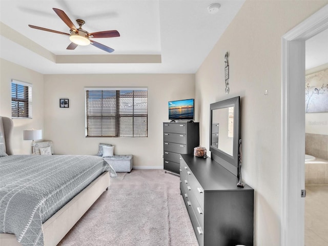 carpeted bedroom with ceiling fan, a raised ceiling, ensuite bathroom, and multiple windows