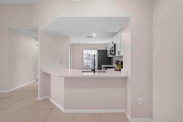 kitchen with kitchen peninsula, appliances with stainless steel finishes, sink, light tile patterned floors, and white cabinets