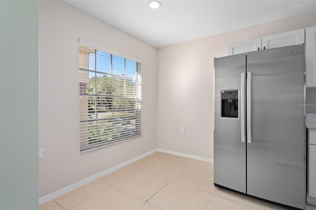 kitchen with stainless steel fridge, white cabinetry, and light tile patterned floors