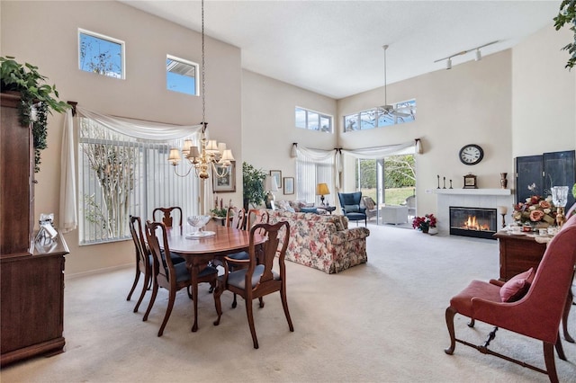 carpeted dining area featuring a fireplace, a high ceiling, track lighting, and an inviting chandelier