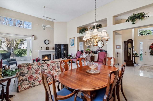 dining space with a fireplace, a high ceiling, ceiling fan with notable chandelier, and light tile patterned floors