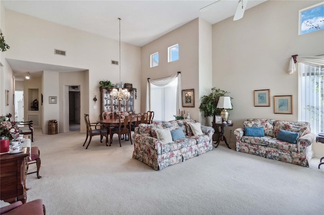 carpeted living room featuring a towering ceiling, a healthy amount of sunlight, and ceiling fan with notable chandelier