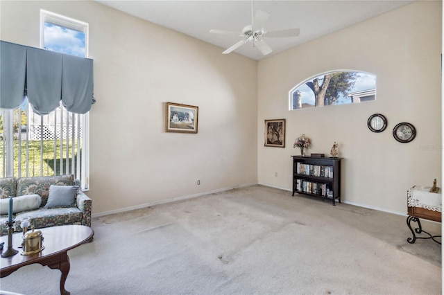 sitting room with ceiling fan, a towering ceiling, light carpet, and a wealth of natural light