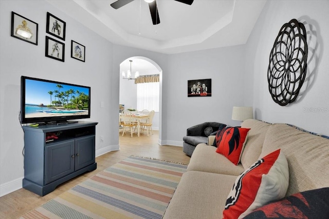 living room with ceiling fan with notable chandelier, a raised ceiling, and light hardwood / wood-style flooring