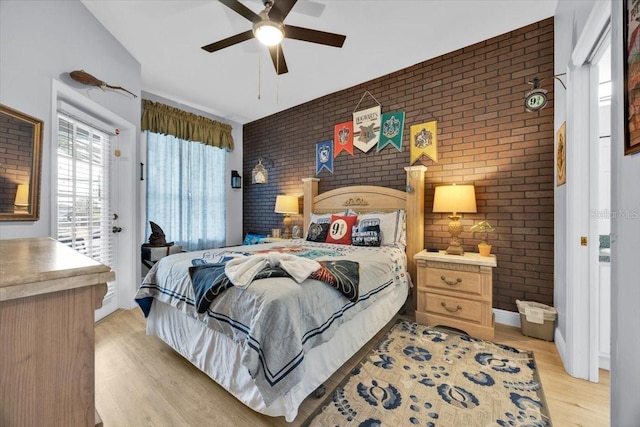 bedroom featuring ceiling fan, brick wall, and light hardwood / wood-style floors