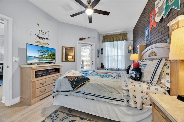 bedroom with ceiling fan, light hardwood / wood-style floors, brick wall, and vaulted ceiling