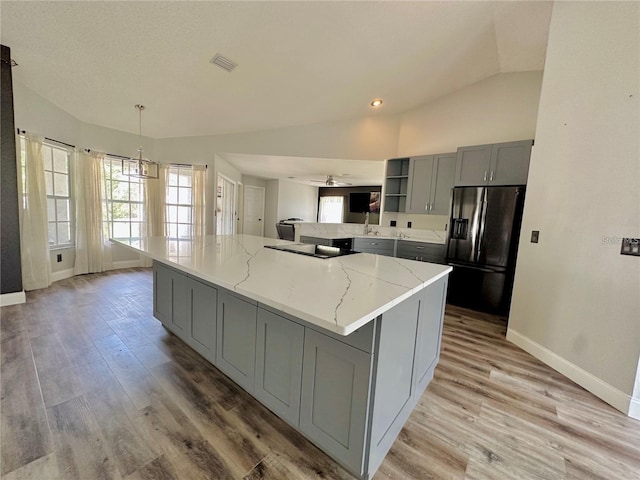 kitchen with gray cabinetry, vaulted ceiling, stainless steel fridge, decorative light fixtures, and light stone counters