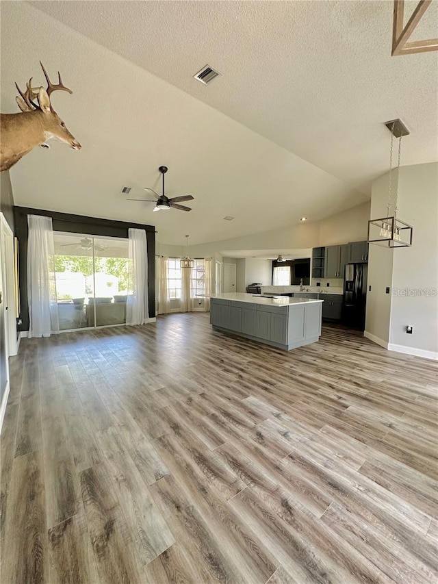 unfurnished living room with ceiling fan, light wood-type flooring, a textured ceiling, and vaulted ceiling