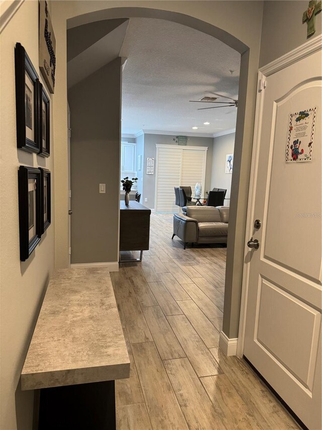 hallway with crown molding, light hardwood / wood-style floors, and a textured ceiling