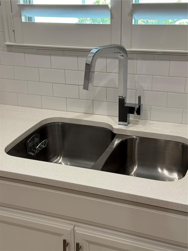 interior details with decorative backsplash, light stone countertops, and sink