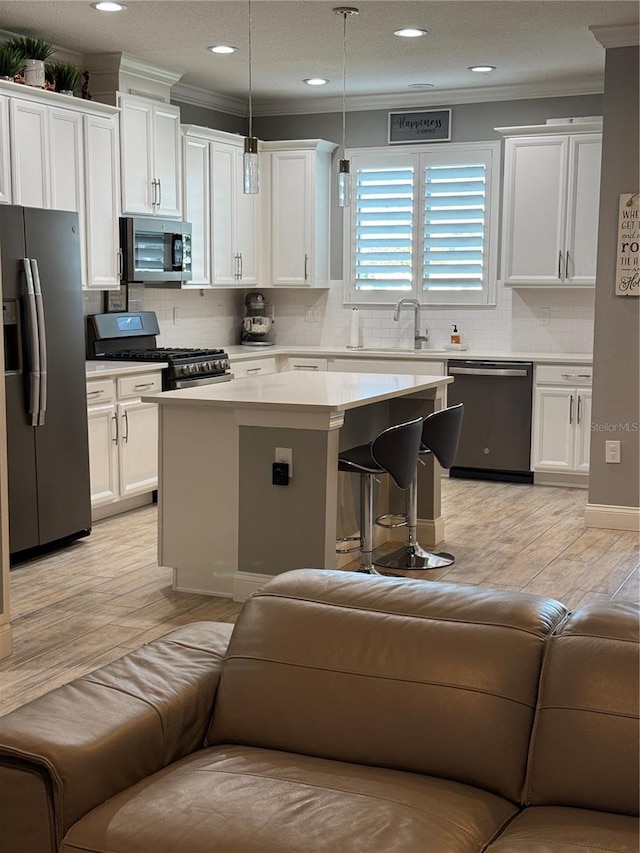 kitchen with decorative light fixtures, stainless steel appliances, a kitchen island, and white cabinetry