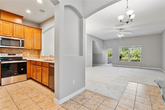 kitchen featuring tasteful backsplash, ceiling fan with notable chandelier, stainless steel appliances, light tile patterned floors, and hanging light fixtures