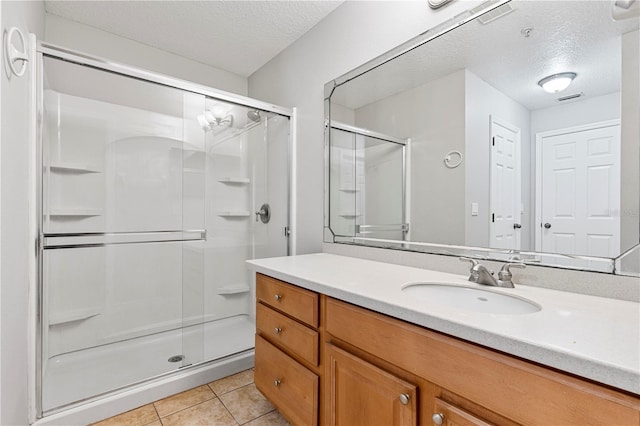 bathroom with tile patterned floors, vanity, a shower with shower door, and a textured ceiling