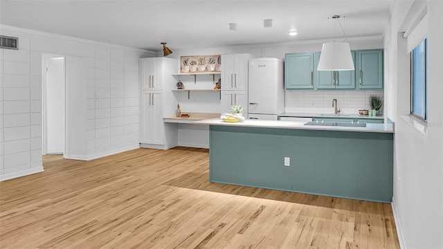 kitchen featuring kitchen peninsula, light wood-type flooring, crown molding, sink, and pendant lighting