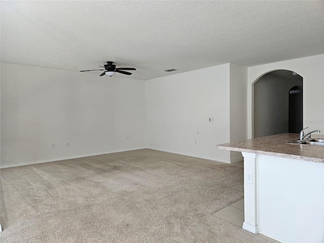 unfurnished living room featuring light carpet, sink, ceiling fan, and a textured ceiling