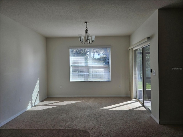 carpeted empty room with plenty of natural light, a textured ceiling, and an inviting chandelier