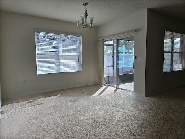 empty room featuring carpet, a textured ceiling, and an inviting chandelier