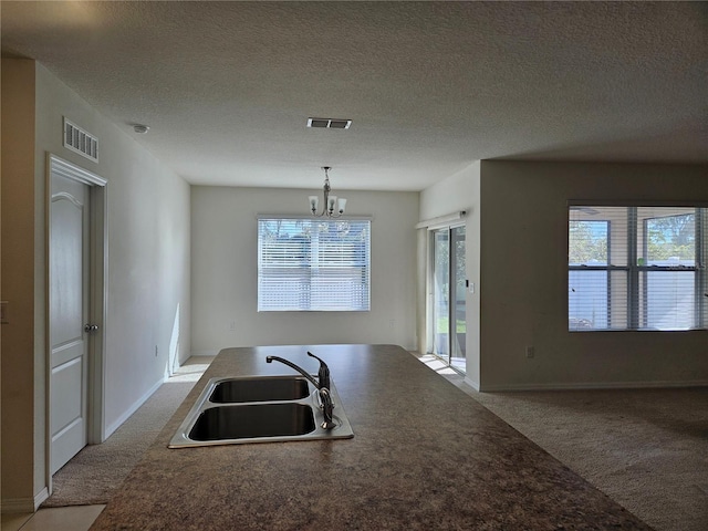 kitchen featuring a textured ceiling, light colored carpet, sink, pendant lighting, and a notable chandelier