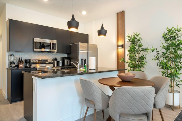 kitchen featuring sink, hanging light fixtures, light hardwood / wood-style flooring, tasteful backsplash, and stainless steel appliances