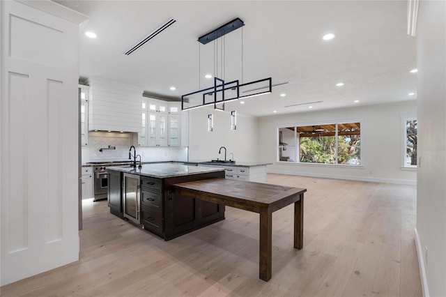 kitchen with light stone counters, hanging light fixtures, light wood-type flooring, a kitchen island with sink, and white cabinets