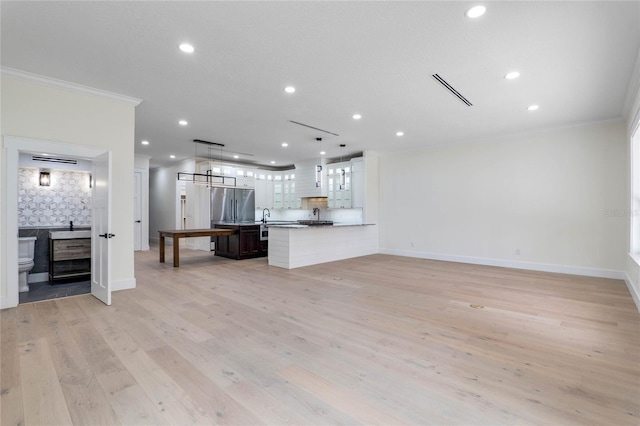 kitchen featuring stainless steel fridge, hanging light fixtures, kitchen peninsula, crown molding, and light wood-type flooring